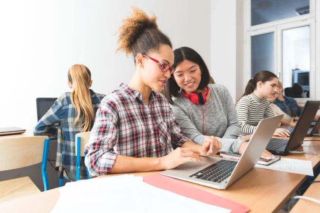 Estudantes de faculdade estudando e colaborando em sala de aula com laptops e livros, ambiente acadêmico para aprimorar conhecimentos e habilidades.